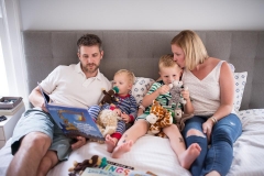 Grand Rapids family documentary photographer captures photograph of family cuddling and reading books in bed