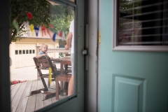 Child in a highchair peers through the door during a documentary family session near Grand Rapids