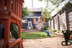 Documentary photography image of a boy swinging over a sandbox while his family approaches in background