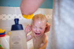 Boy in bathtub cries while mother washes his hair during a family documentary photography session