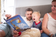 Dad reads book to laughing child while mother looks on during a family photography documentary session