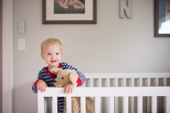 Boy in crib grins at family documentary photographer near Grand Rapids