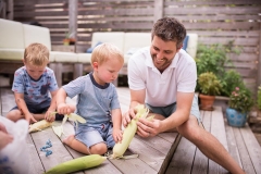 Father shucks sweet corn with sons during a documentary family photography session in East Grand Rapids