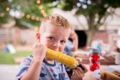 Documentary family photograph of young boy biting into corn on the cob