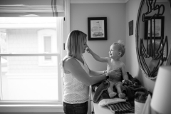 Boy pinches mothers nose while she dresses him in this family documentary photography picture