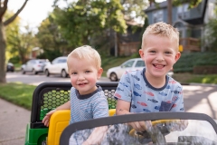 Boys in a motorized car grin at family documentary photographer during East Grand Rapids family walk