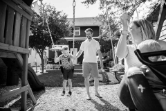 Black and white documentary style family photo of father pushing son on a swing