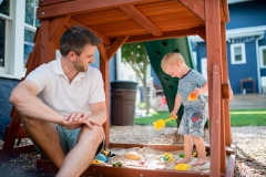 Father and son play in sandbox while a documentary photographer captures day in the life pictures