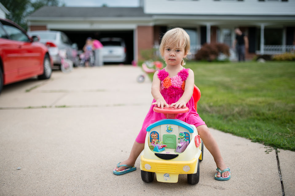 Girl astride a toy car in front of their Grand Rapids home for documentary family session