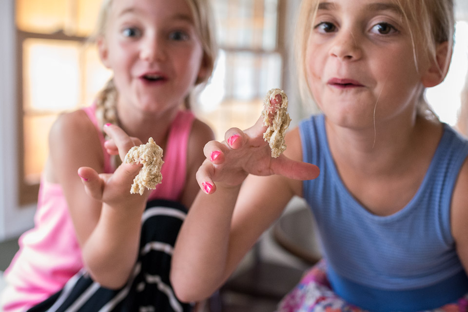 Two girls display cookie dough covered fingers to family documentary photographer during a family session