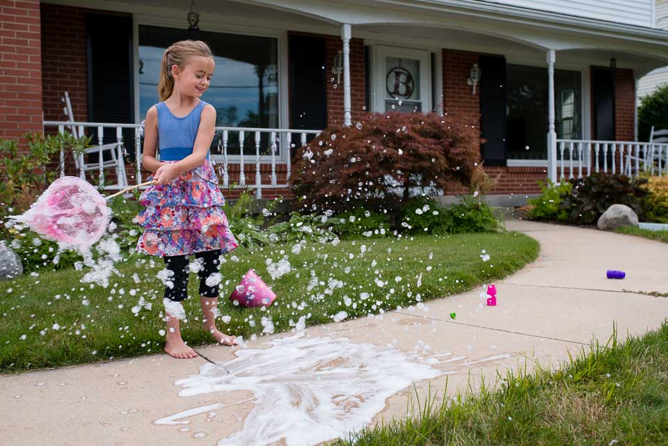 Girl waves a net to create bubble foam during a family documentary session