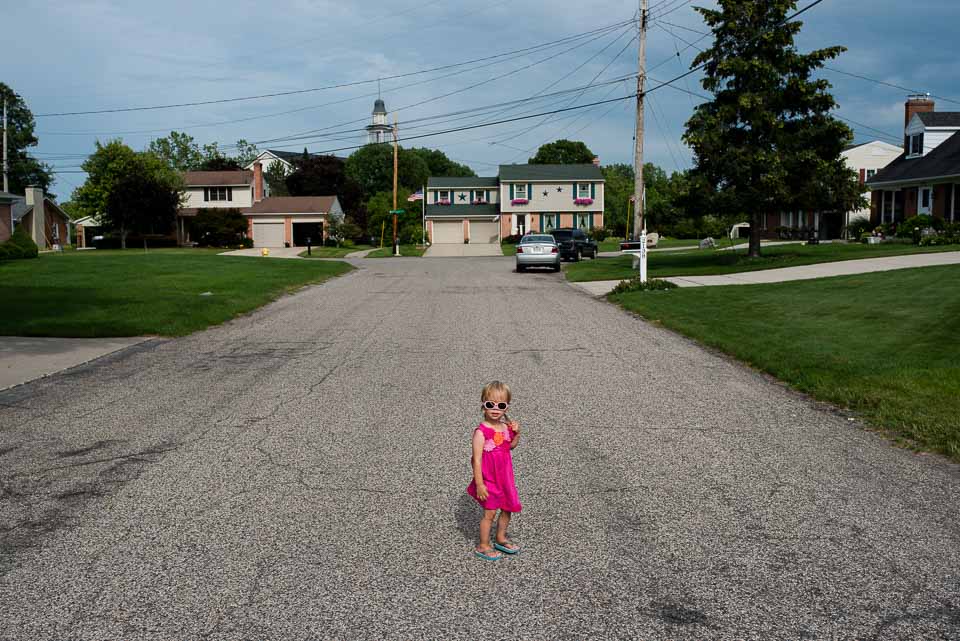 Small child wears sunglasses and stands in the road during a family photojournalism session