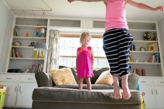 Sisters jump from the couch in a West Michigan family documentary photography session