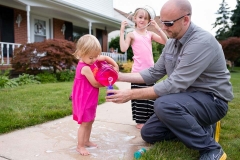 Father in work clothing assists child pouring bubble solution during documentary family photography session