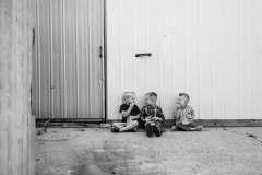 Three young boys sit against a barn and chat a candid lifestyle portrait