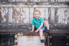 A young boy sits in a jaunty pose and grins at the camera in this urban Grand Rapids child portrait