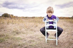 A portrait of a serious boy sitting on a white chair in a fall Michigan field