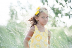 A young girl with windblown hair stands in beach grass at Lake Michigan