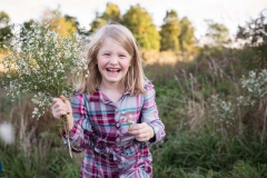 A girl holds wildflowers and laughs while looking into the camera