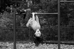 A black and white image of a laughing girl hanging upside down at a playground