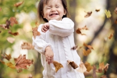 Fall leaves float around a girl laughing delightedly at Aquinas College