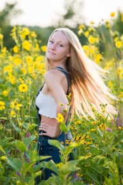 Senior portrait girl twirls her hair in a backlit field of summer flowers