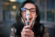 Artistic senior girl laughs as she holds up paint brushes for senior portraits in Grand Rapids