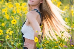 Senior portrait girl twirls her hair in a backlit field of summer flowers