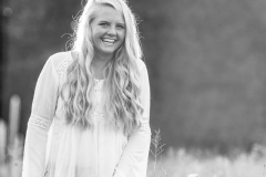 Senior girl poses for pictures in a backlit summer field of flowers near Grand Rapids