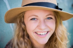 Senior girl wearing a straw hat smiles in an urban Grand Rapids senior picture