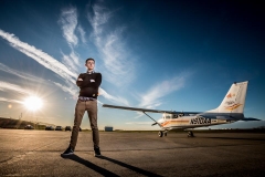 High school senior guy poses on the tarmac with an airplane for Grand Rapids senior portraits